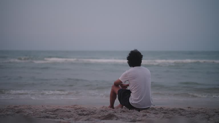 Rear view of a man sitting alone by the sea in the evening