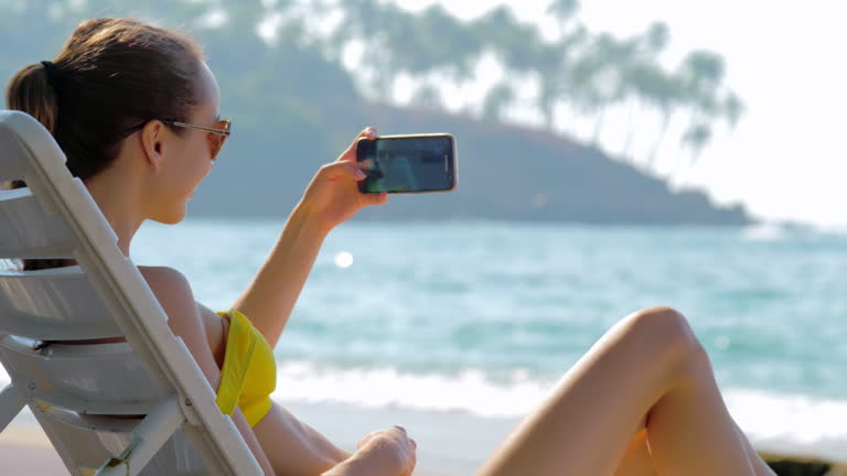 Woman takes selfie with phone while relaxing on tropical shore