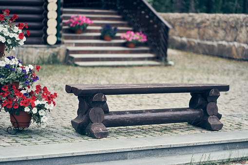 An old dark and low wooden bench on the background of a wooden ladder. There are pots of petunia flowers on the ladders. High quality photo