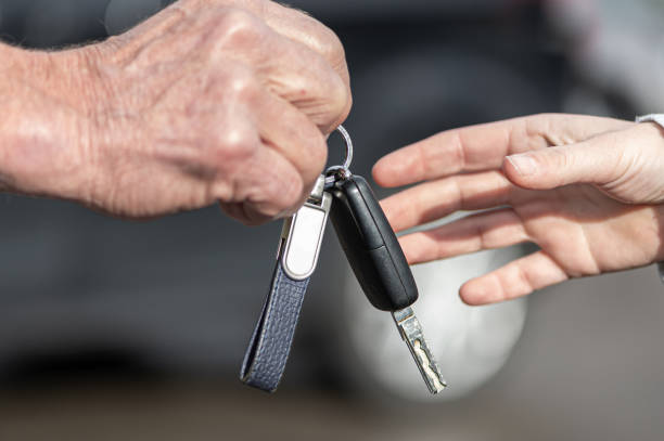 A businessman hands over a car key to a woman in front of a blurred car A businessman hands a woman a car key in front of a blurred car car key stock pictures, royalty-free photos & images
