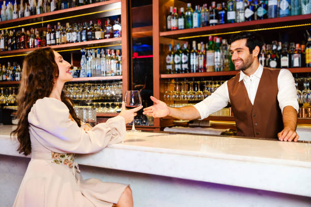 istock Caucasian professional bartender or mixologist making a cocktail for women at a bar. An attractive barman served a glass of wine with a smile to a woman. Bartender service at the night club restaurant 2150955219