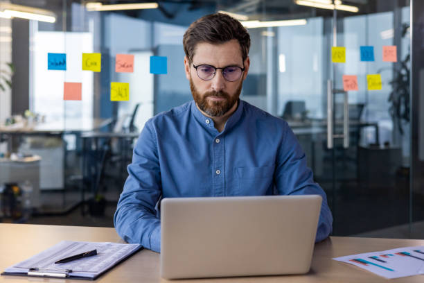 istock Portrait of a serious and focused young specialist, developer and programmer sitting in the office at the table and working on a laptop 2150956620