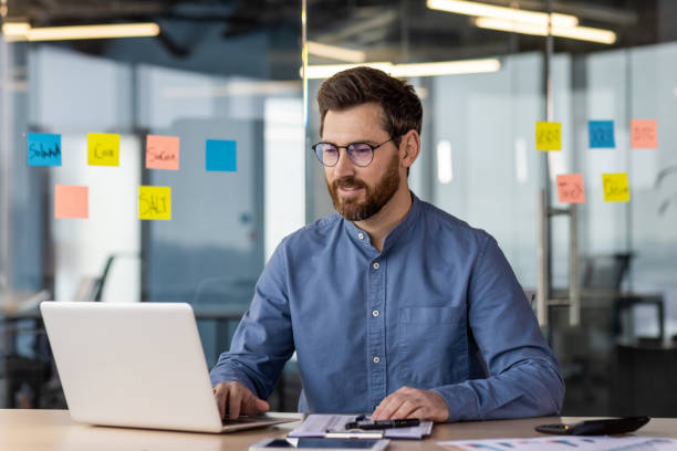 istock Successful and self-confident young businessman working concentratedly in the office behind a laptop. Sitting at the desk smiling, checking data and accounts, talking on a video call 2150957398