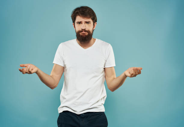 istock A man in a white T-shirt and with a thick beard on a blue background gestures with his hands 2150957560