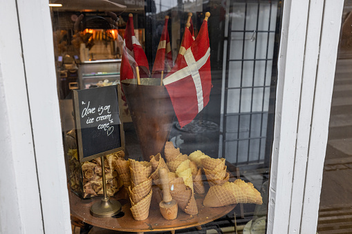This charming stock image captures a cozy ice cream shop display, featuring an array of fresh waffle cones and the Danish flag, symbolizing national pride. The sign humorously advertises 