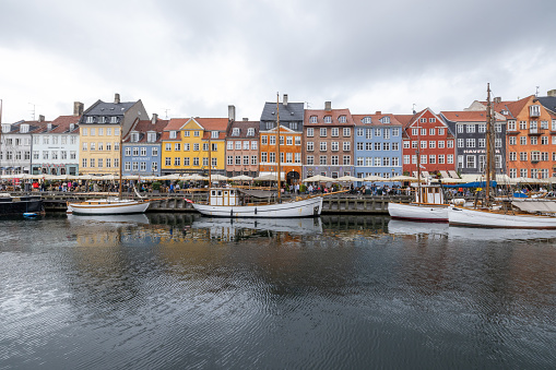 This engaging image features the picturesque Nyhavn district in Copenhagen, known for its vividly colored buildings and historical wooden boats moored along the canal. The scene captures a typical overcast day, filled with tourists and locals enjoying the charming atmosphere along the waterfront. This area is a popular destination for its vibrant architecture, cultural history, and lively dining scene, making it a quintessential symbol of Danish urban life.