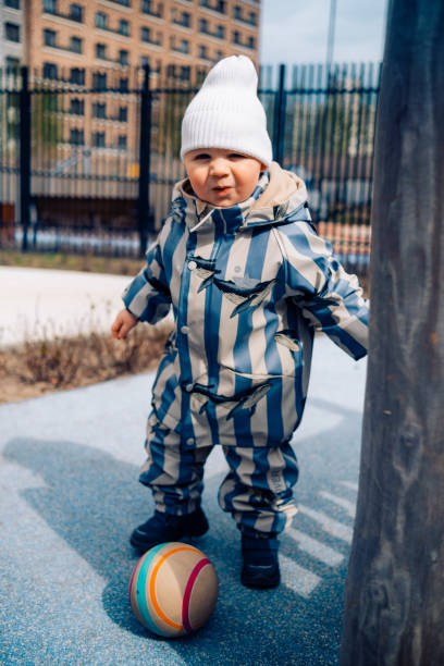 istock A boy child in striped overalls falls while playing with a ball. Kid aged about two years 2150959905