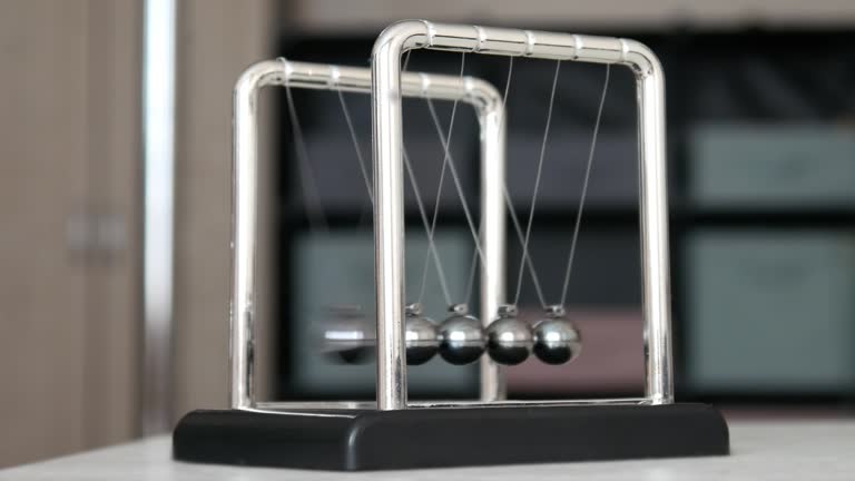 A Newton's cradle on the table close-up and a child's fingers pulling back one sphere and starting the pendulum