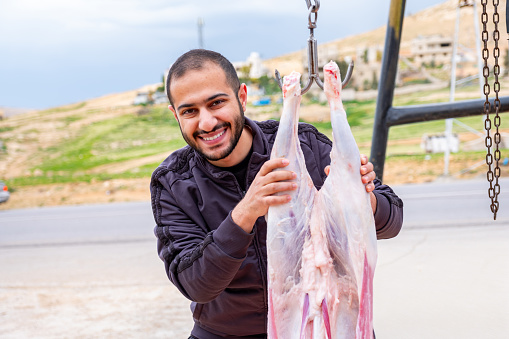 A man is posing for a photo with his sheep after removing its skin, thanking Allah for providing food during Eid al-Adha