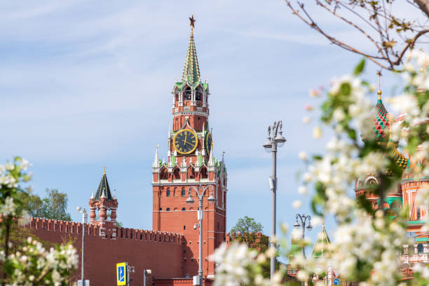 Spasskaya Tower of Moscow Kremlin in a spring day Close-up side view of Spasskaya Tower of Moscow Kremlin in a sunny spring day. White blooming apple tree flowers in the foreground. Soft focus. Russian culture and symbols theme. russia city spring stock pictures, royalty-free photos & images