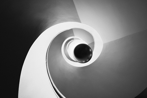 A mesmerizing staircase spirals upwards, bathed in the light of a suspended lamp made up of rings of glass that cascade from the black sphere at its base towards the ceiling.