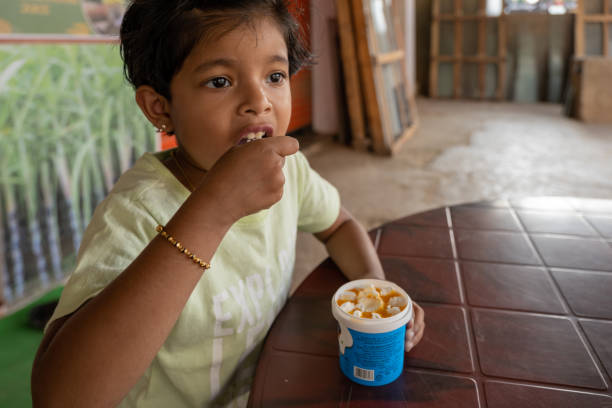 This image is about Kid eating small cup ice cream in wood workshop on plastic table and which was mango flavor