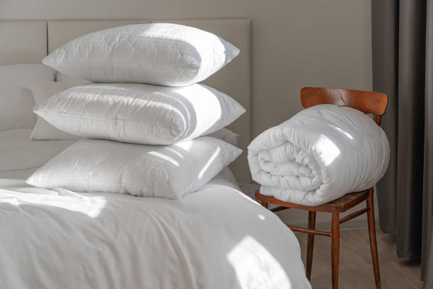 istock A bed with white pillows and a blanket, next to a bedside table with a lamp, daylight 2150985156