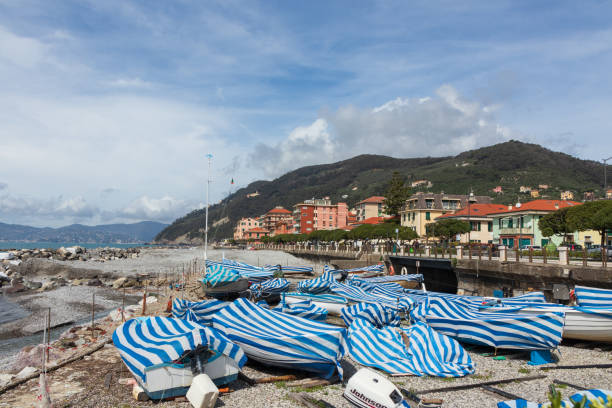 Chiavari, Italy - April 05 2024 - Numerous boats covered with blue and white sheets color Chiavari's waterfront with its many trees and buildings