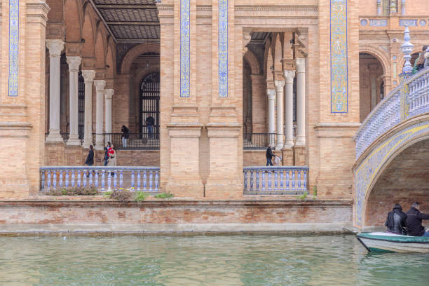 Seville, Spain - December 31, 2023:  The Plaza de Espana, with visitors rowing boat and strolling around in a relatively quiet cloudy afternoon on New Year Eve 2023.  HDR encoded.