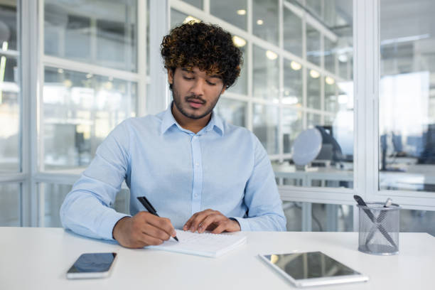 istock Focused young professional man writing in notebook at office 2150991557