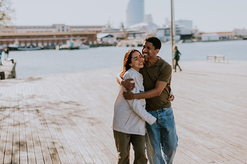 Joyful couple hugs on a pier in Barcelona, with the city skyline softly blurred in the background