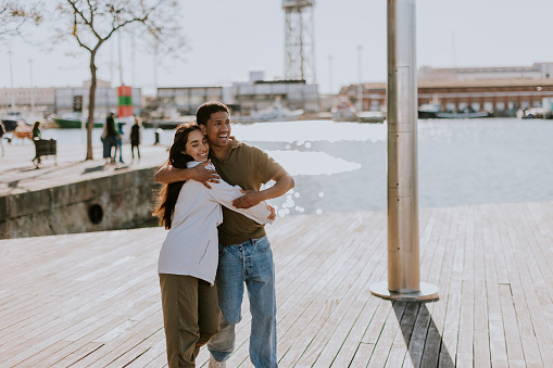 Joyful couple hugs on a pier in Barcelona, with the city skyline softly blurred in the background