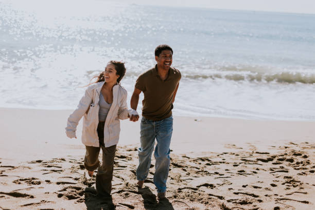 istock Joyful couple running hand in hand along a sunlit beach at sunset 2150994967