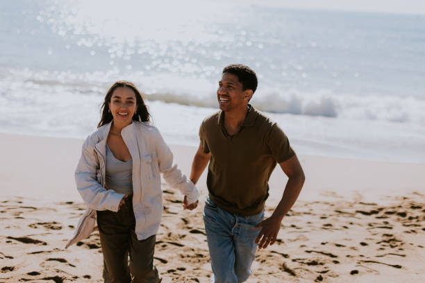 istock Joyful couple running hand in hand along a sunlit beach at sunset 2150994978