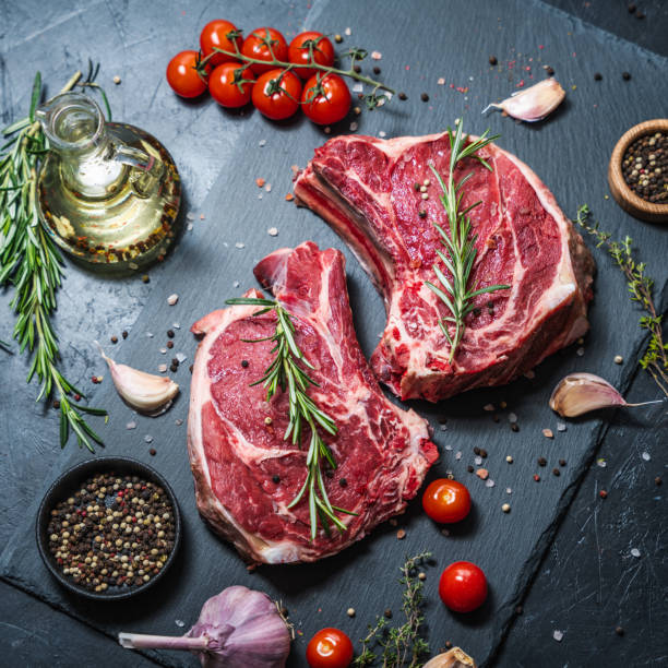 istock Two raw beef steaks on the bone on a black slate serving plate, decorated with ingredients and spices. 2150997251