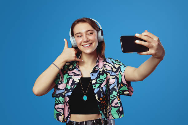 istock Friendly student girl with headphones making selfie with smartphone while showing call me gesture 2150998304