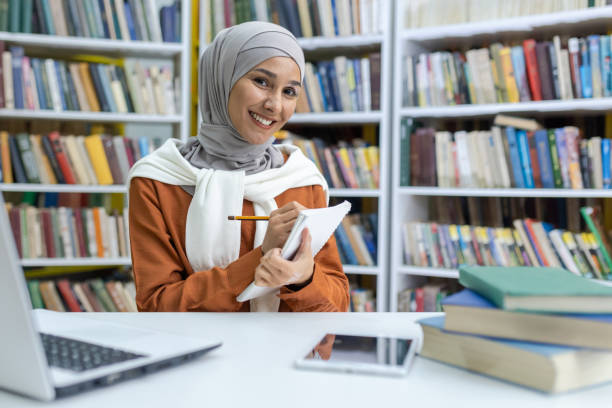 istock Smiling hijab-wearing student studying in library with laptop 2150999483