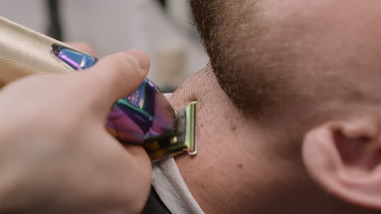 Stylist shaves young man neck using trimmer in barbershop