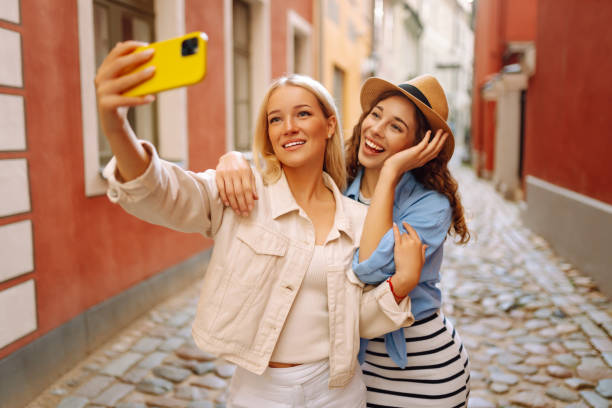 istock Two beautiful  woman friends walking together around the city, using smartphone while making selfie. 2151001261