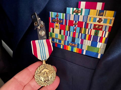 An unidentified person holds a newly awarded Defense Meritorious Service Medal to a U.S. Air Force service member who displays a variety of existing ribbons and devices on their “Class A” uniform coat.