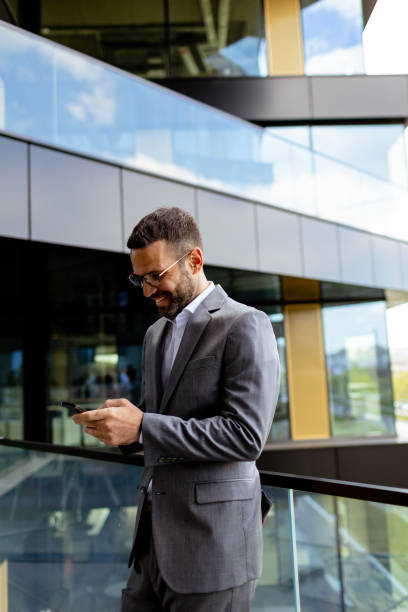istock Confident Businessman Smiling in Sharp Suit Against Modern Glass Office Facade 2151003728
