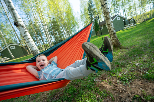 Playful boy in the hammock at campsite at sunny day