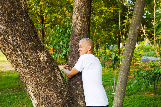 istock Thai senior man smiling and embracing a tree trunk 2151006340