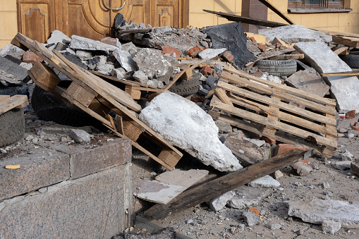 A pile of construction waste near a building renovation: boards, pallets, tires, broken bricks and concrete slabs