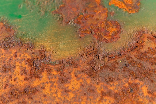 Interesting structural background of a rusty metal surface, shot close-up, partially painted green with oil paint, large pieces of rust, unusual bright pattern, natural aging, bright color, vintage look.
