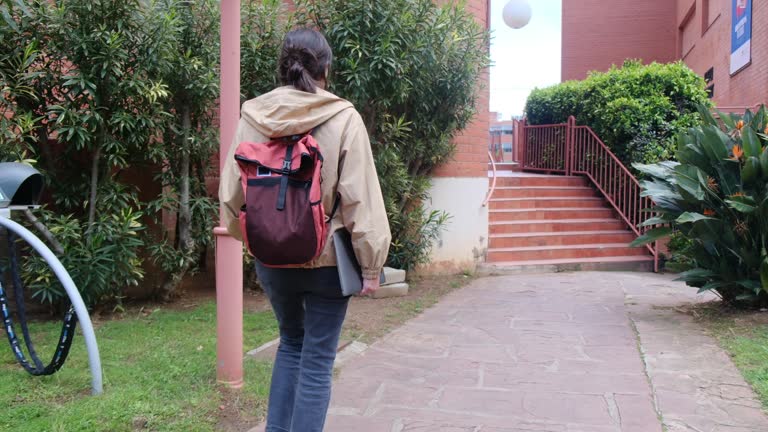 A Latina student navigates the university grounds, laptop, and backpack in tow, under the radiant sun, en route to classes. College life, aspirations, educational journey.