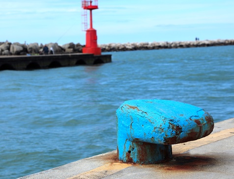 large blue bollard that serves to securely moor ships to the port and a red lighthouse in the background