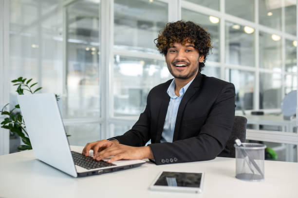 istock Arab businessman keeping hands on keyboard of portable computer while looking at camera with toothy smile. Curly employer feeling ready starting new productive and profitable week in office 2151016369