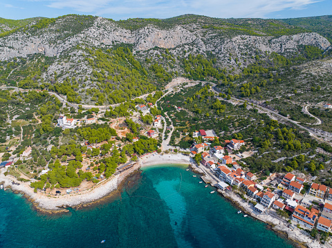 AERIAL: Scenic shot of a small beachfront settlement on a Croatian island Hvar. Flying over the small picturesque bay of a remote village with small colorful houses and campers hidden beneath trees.