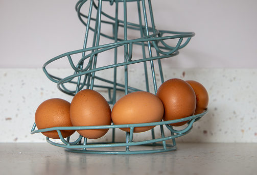 Brown eggs nestled in a turquoise wire basket on a kitchen countertop against a plain background