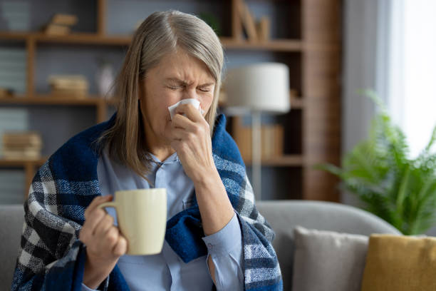 istock Senior woman sneezing while holding a mug at home 2151023154