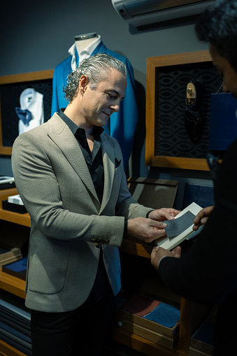 A happy and smiling businessman in a suit inspects fabrics for a new suit at his personal tailor