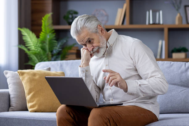 istock Senior man with beard using laptop on a comfortable sofa at home 2151032753