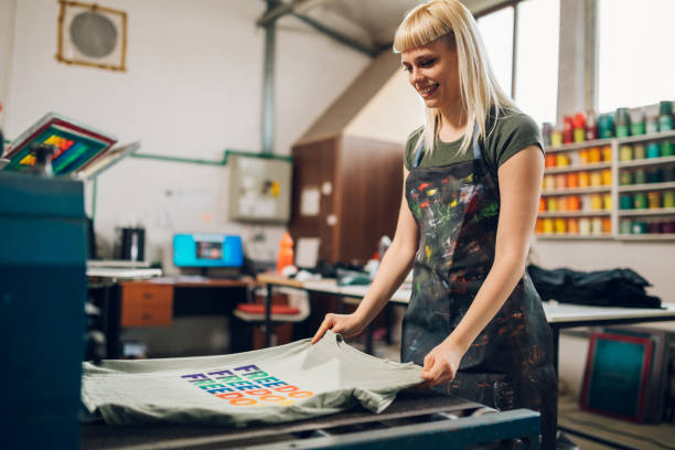 istock Print shop worker putting screen printed t-shirt into drying machine. 2151033679