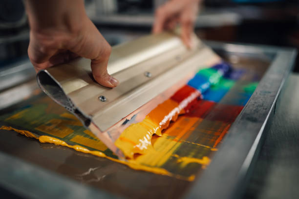 istock Close up of print shop worker's hands using squeegee for screen printing 2151033685