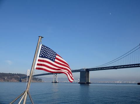 San Francisco - January 3, 2012: A U.S. flag flutters in the breeze on the back of ferry boat with a clear blue sky backdrop and a famous suspension Bay Bridge in the distance.