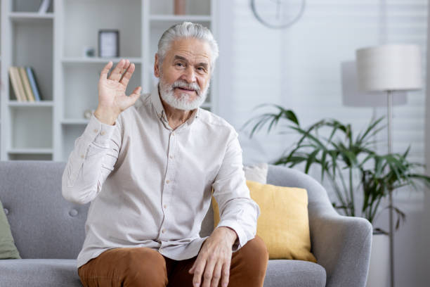 istock Senior man on a video call waving at the camera from home 2151038651