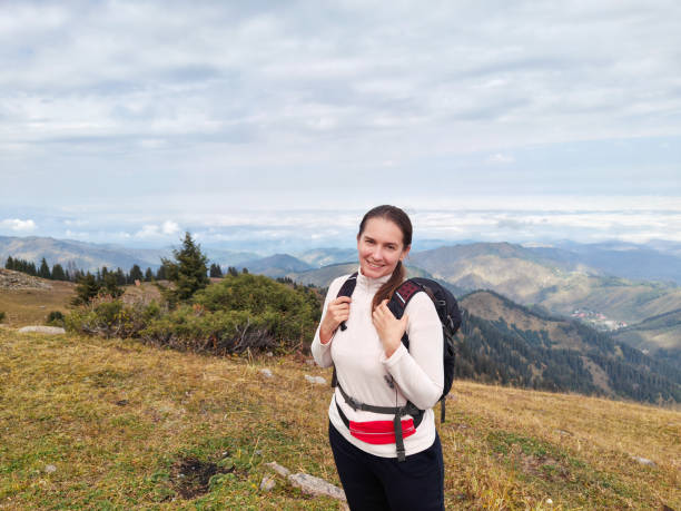 istock Smiling woman hiker with a backpack standing on a mountain overlooking distant hills 2151040901