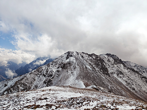 Snow-dusted mountain ridge with rugged terrain under a cloudy sky.