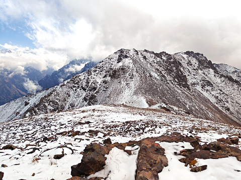 Snow-dusted mountain ridge with rugged terrain under a cloudy sky.